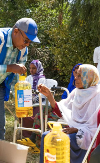 Smiling Ethiopian women receiving a food parcel from an Islamic Relief Ethiopia aid worker.